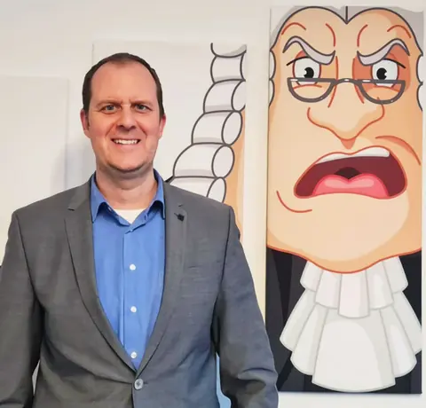 Rechtsanwalt Fabian Schilling vor einem Karikatur-Gemälde
