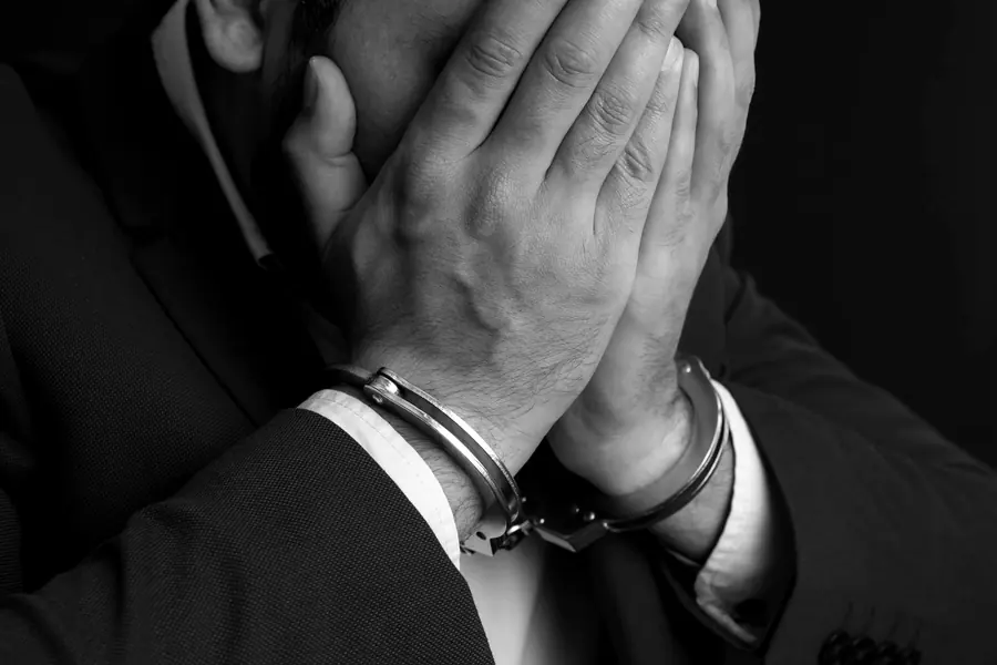Mann mit Handschellen verbirgt sein Gesicht hinter den Händen
